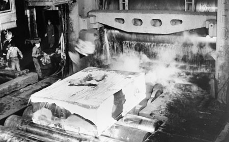 Rock salt and burlap bags are tossed onto an ingot to break the slag off the exterior as it passes through the rolls of the mill. — Hagley Museum & Library