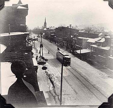 Main Street, looking east from a point near the Thompson Building.  A trolley car makes its way through the snow-packed road, while a horse and cutter wait along the curb.